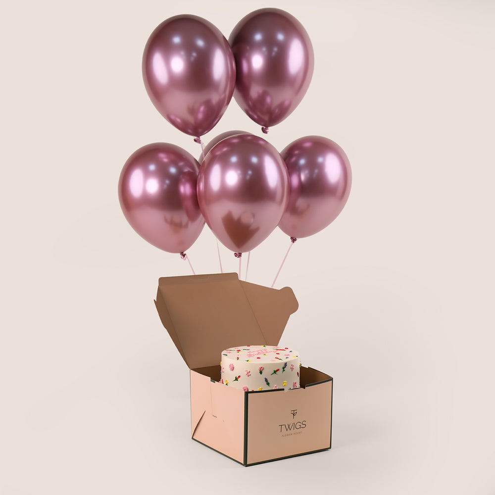 A 2kg floral birthday cake with intricate icing details, bundled with six metallic pink balloons, placed inside a brown box with a 'Happy Birthday' message.