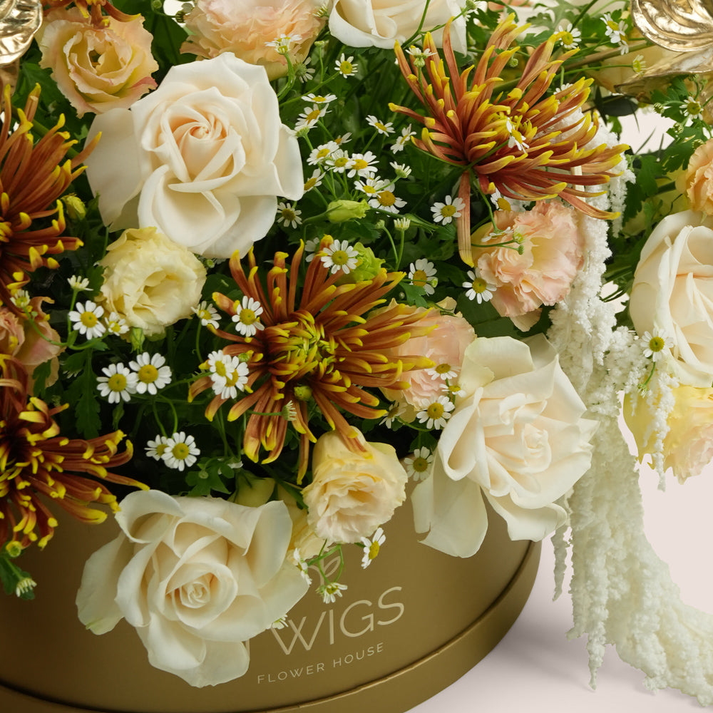 Aurelia, a luxury flower arrangement of white garden roses, saffina chrysanthemums, lisianthus, and gold painted anthurium leaves in a round TWIGS Gold box, with matching gift card.