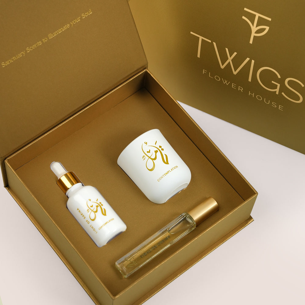 A luxury gift set from Twigs Flower House, featuring Contemplation Gift Set by Light of Sakina, a white essential oil dropper bottle, a white candle jar, and a clear glass perfume rollerball inside a gold presentation box.
