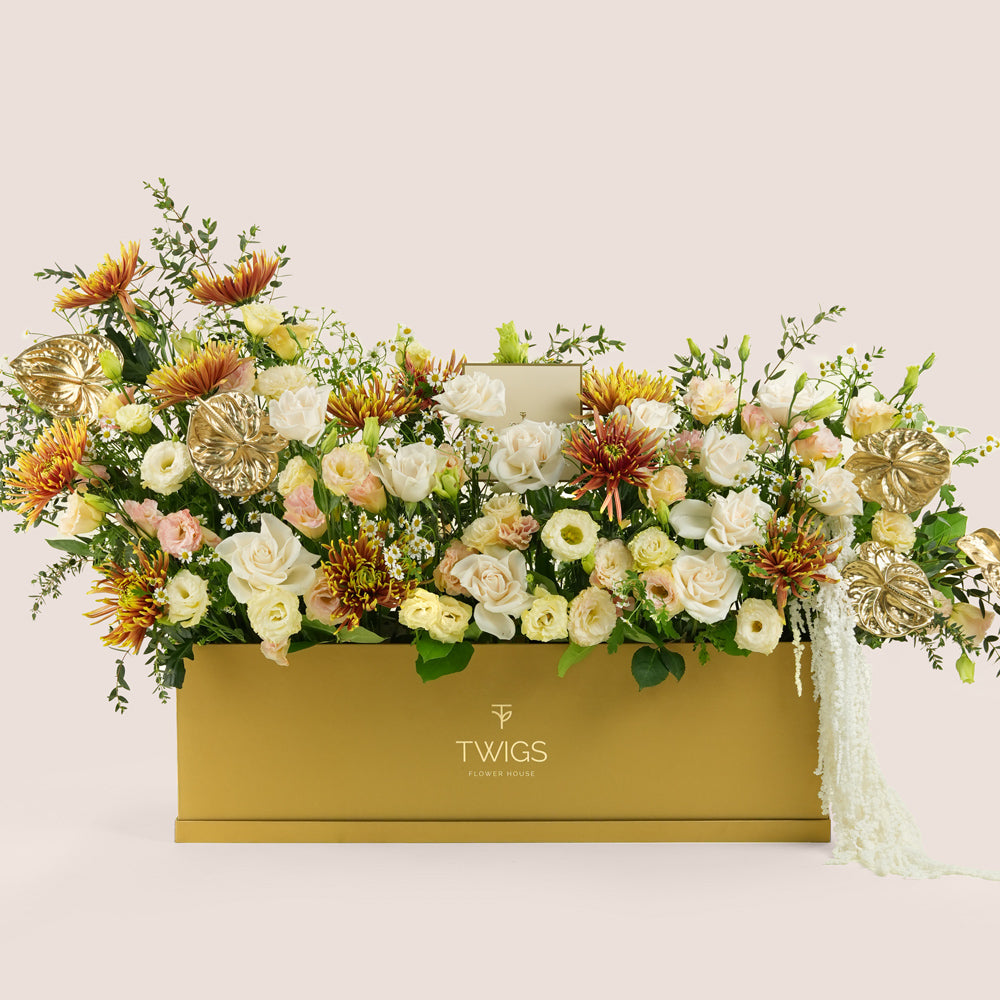 Aurelia, a luxury floral arrangement of white roses, chrysanthemums, lisianthus, and gold painted anthurium leaves in a rectangular TWIGS Gold garden box, with matching gift card.