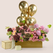 Isadora Celebration, a luxury TWIGS Gold Garden box arrangement of pink and burgundy hydrangeas, garden roses, and green anthurium leaves, paired with a 1kg cake and six gold chrome balloons.