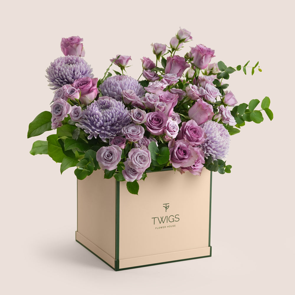 Purple roses and lilac chrysanthemums in shades of lavender arranged in a beige TWIGS Flower House tall box