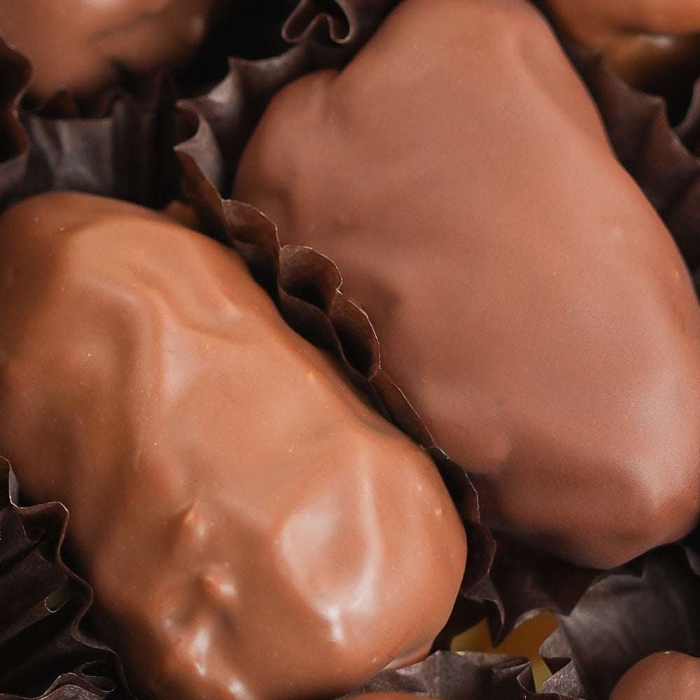 Close-up of milk-chocolate-covered confection pieces in dark paper cups, filling the frame.