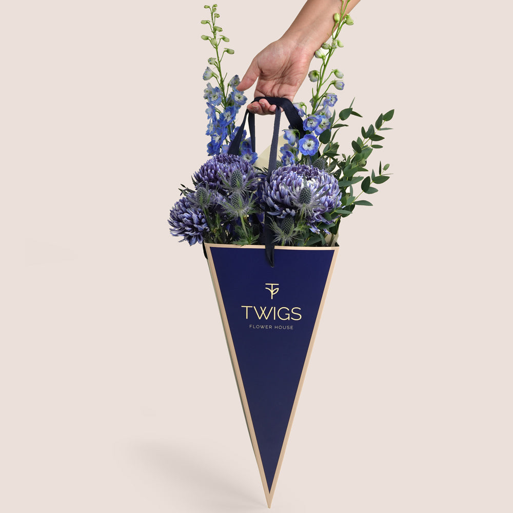 Indigo Carry — blue delphiniums, chrysanthemums and eryngiums in a TWIGS navy cone carry bag, Father's Day blue flower arrangement Dubai