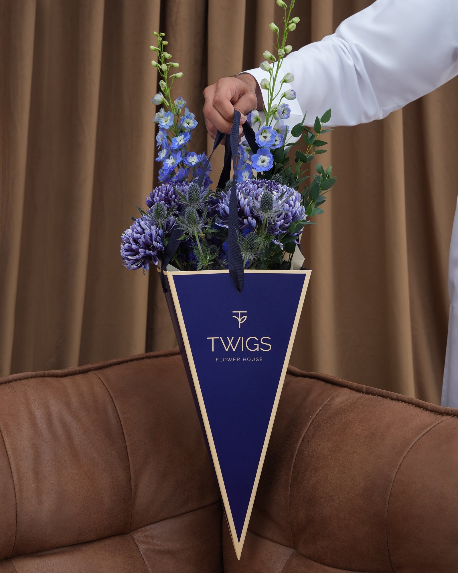 Indigo Carry — blue delphiniums, chrysanthemums and eryngiums in a TWIGS navy cone carry bag, Father's Day blue flower arrangement Abu Dhabi