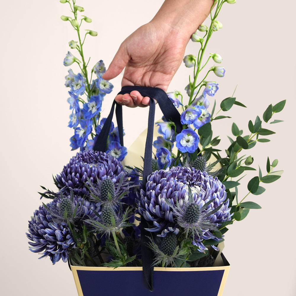 Indigo Carry — blue delphiniums, chrysanthemums and eryngiums in a TWIGS navy cone carry bag, Father's Day blue flower arrangement UAE