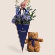 Indigo Carry & Bear — blue delphiniums, chrysanthemums and eryngiums in a TWIGS navy cone carry bag with classic TWIGS teddy bear with blue ribbon, gift for him, gift for baby boy Dubai