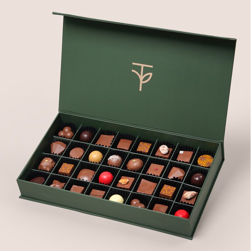 Open green chocolate box with various chocolates on a light gray background