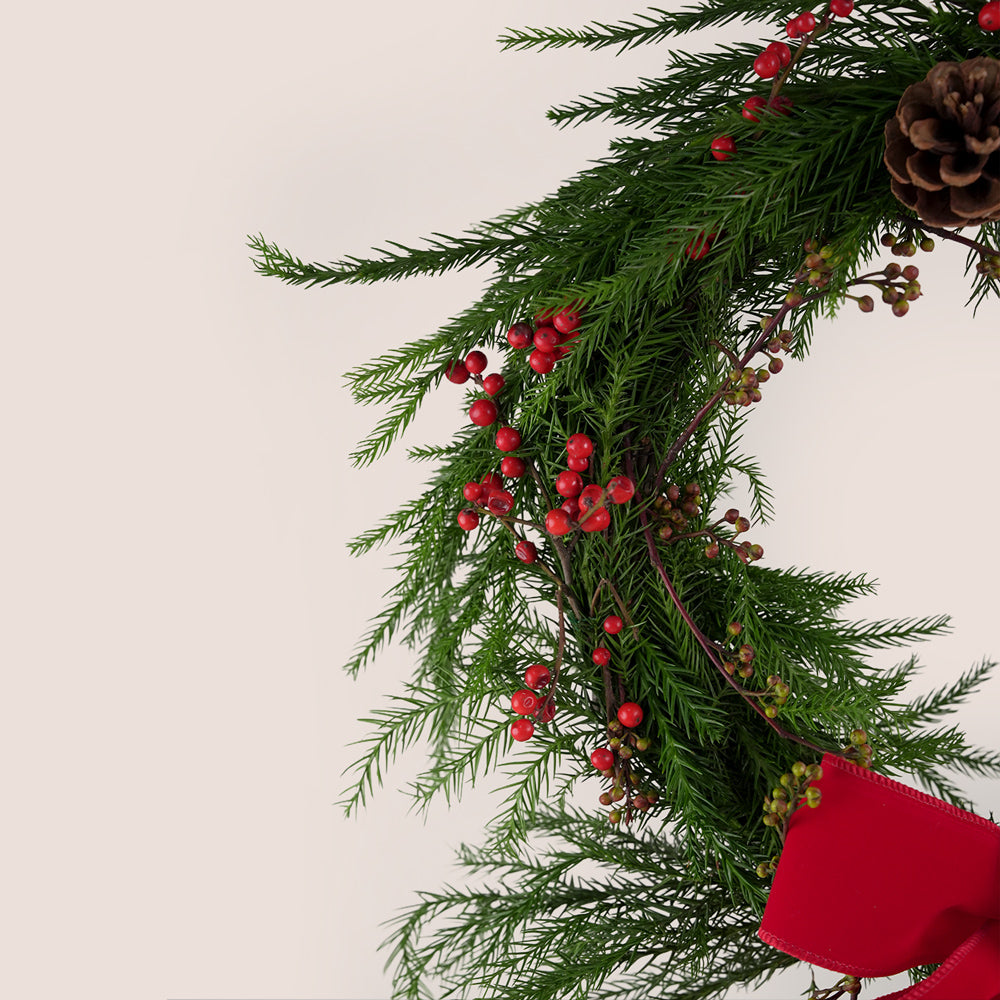 Christmas wreath with greenery, red berries, and pinecones on a light background