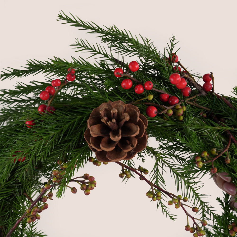 Decorative arrangement of greenery with red berries and pine cones on a beige background