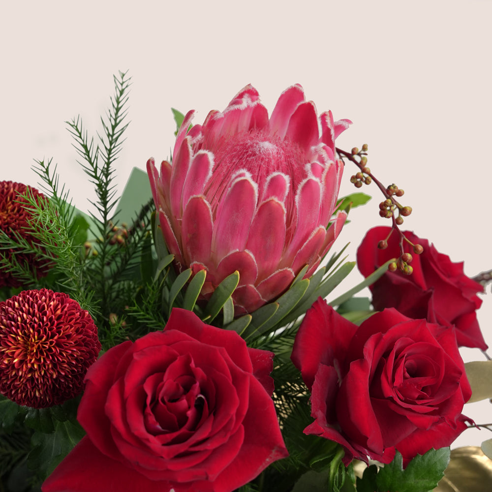Bouquet of red roses and a large pink protea flower with greenery on a light background