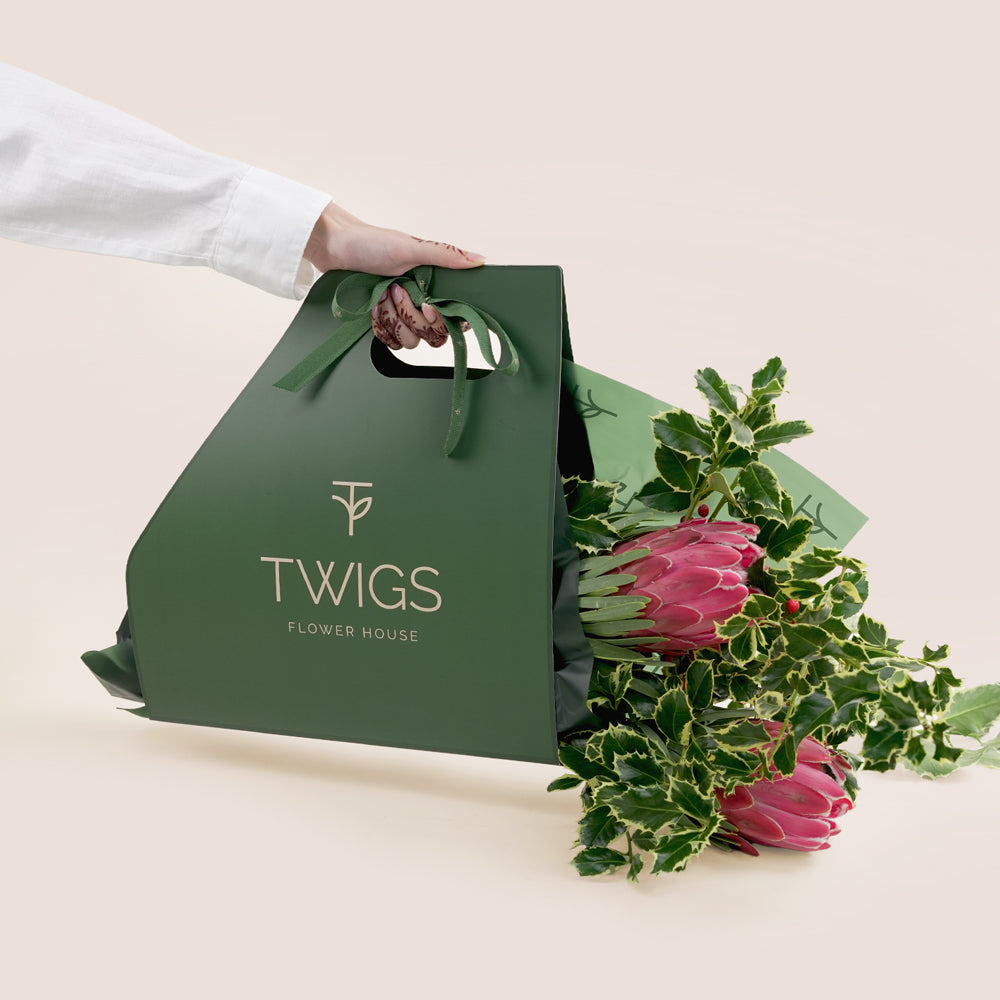 Green floral bag with 'TWIGS' branding and a bouquet of flowers on a light background