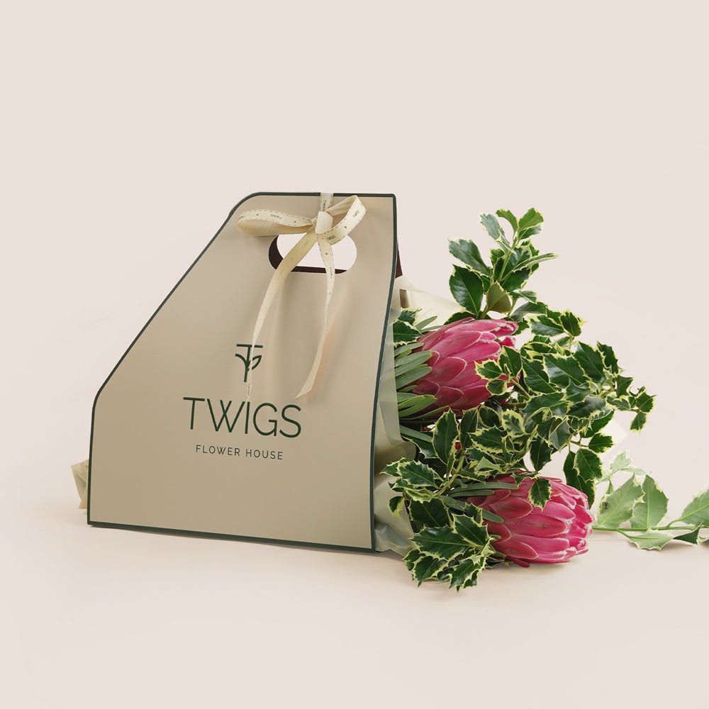 Floral arrangement with a 'TWIGS Flower House' branded gift bag on a light background