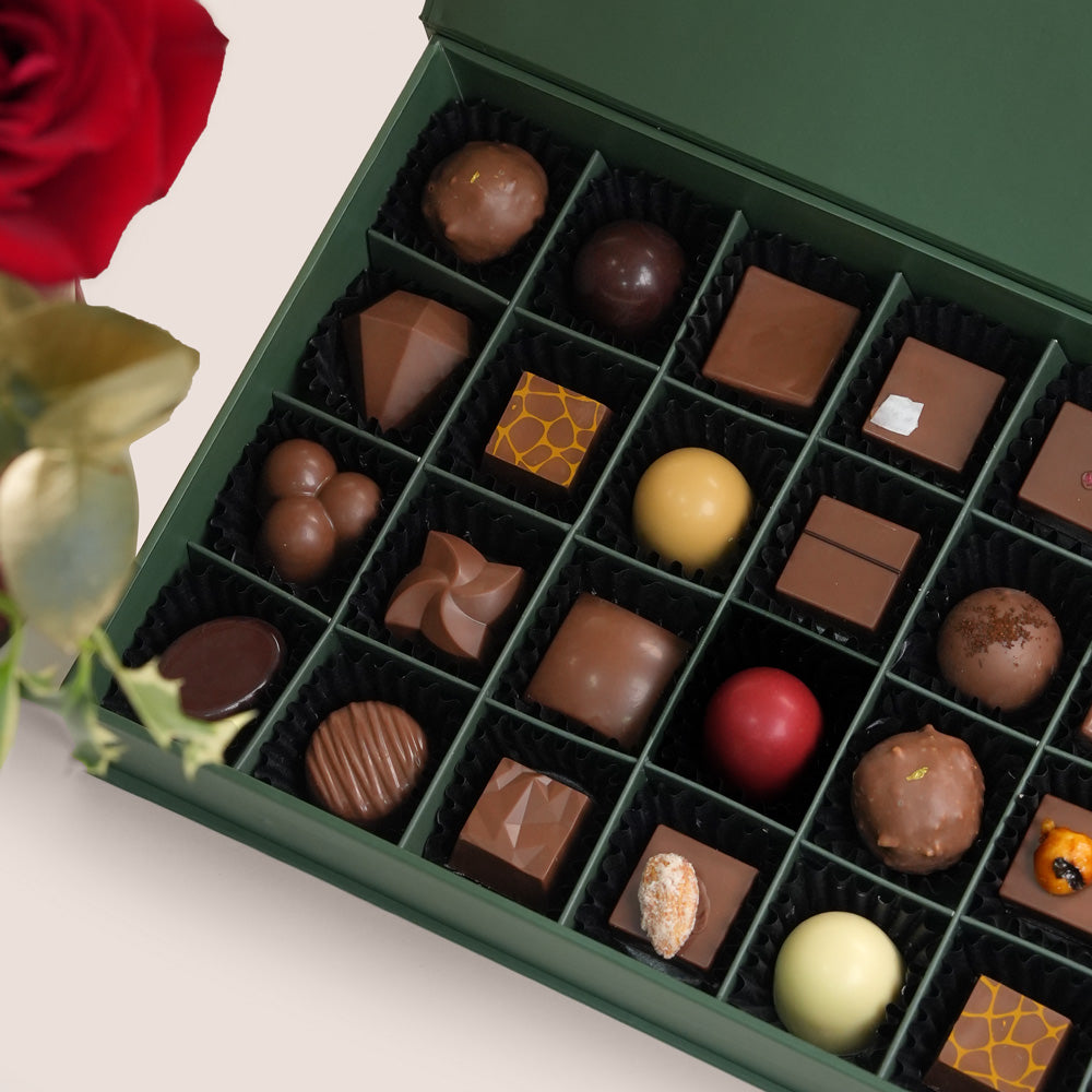 Assorted chocolates in a green box with a red rose on a light background