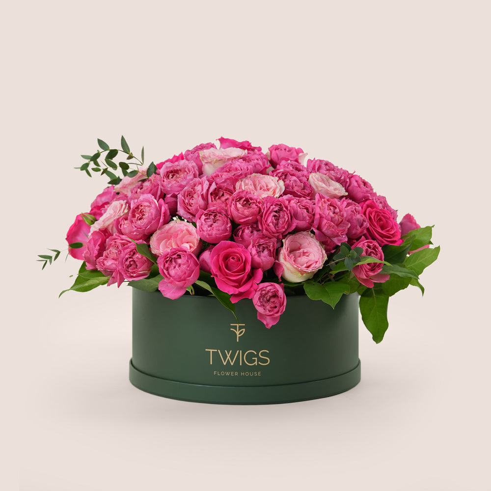 Grande round flower box with fuchsia cerise spray roses, fuchsia Ecuador garden roses, and light pink garden roses in TWIGS beige or green packaging, available for same day flower delivery in Dubai when you buy flowers online.