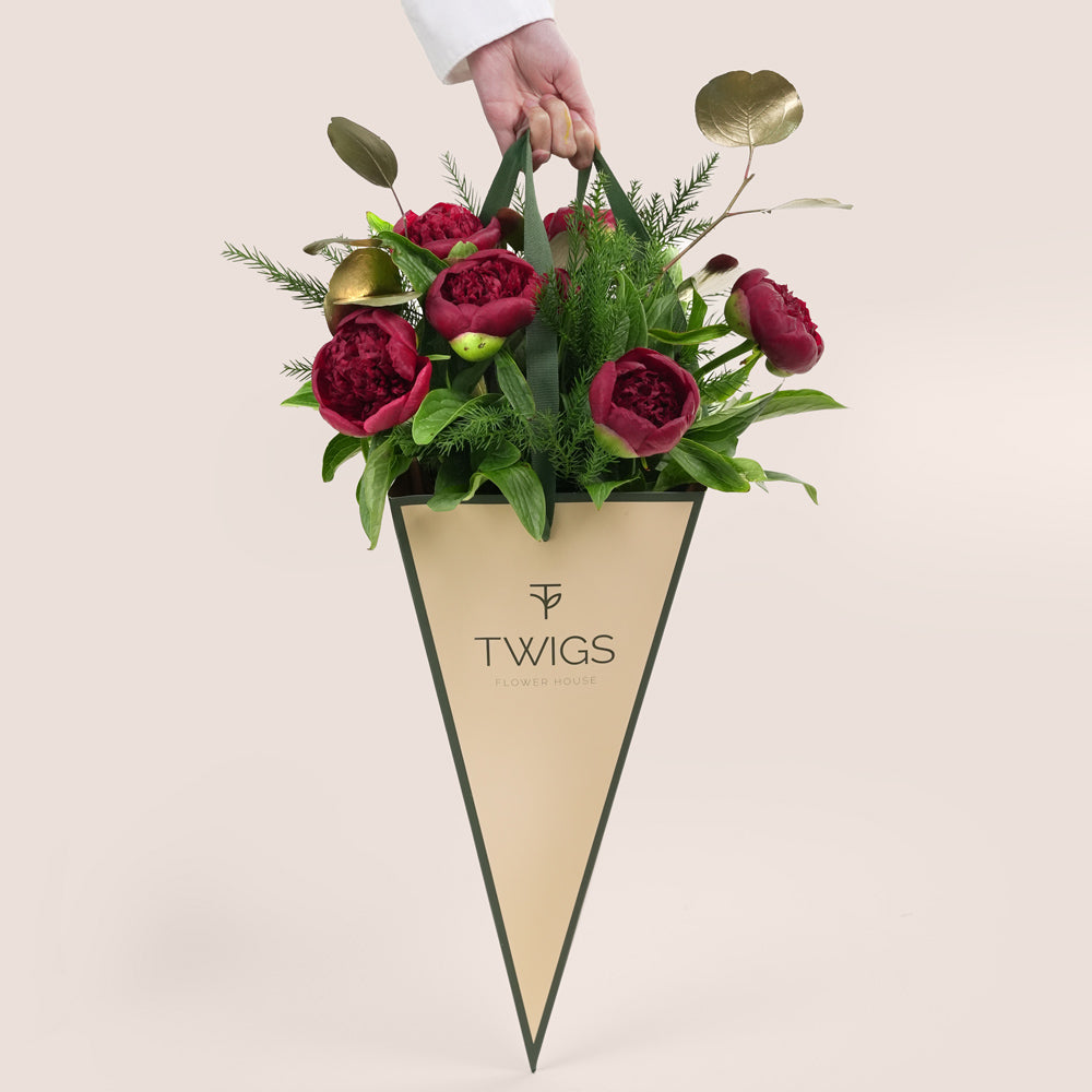beautiful Christmas bouquet of deep red peonies, lush green pine needles, and gold-painted foliage, presented in a distinctive green TWIGS Flower House cone carrier bag.