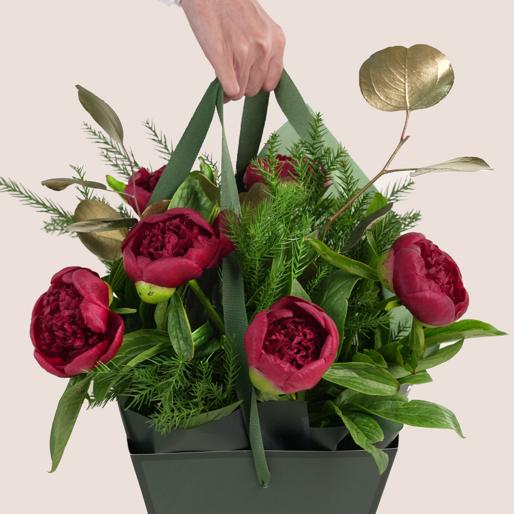 beautiful Christmas bouquet of deep red peonies, lush green pine needles, and gold-painted foliage, presented in a distinctive green TWIGS Flower House cone carrier bag.