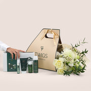 Cosmetic set with 'TWIGS' branding, including bottles and a box, next to a bouquet of flowers on a light background.