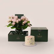 A bundle of a floral cake with colorful icing and a vase of pink roses, both presented in a green box with the TWIGS brand .