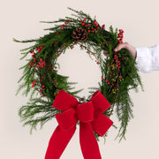Christmas wreath with red bow held by a hand on a beige background