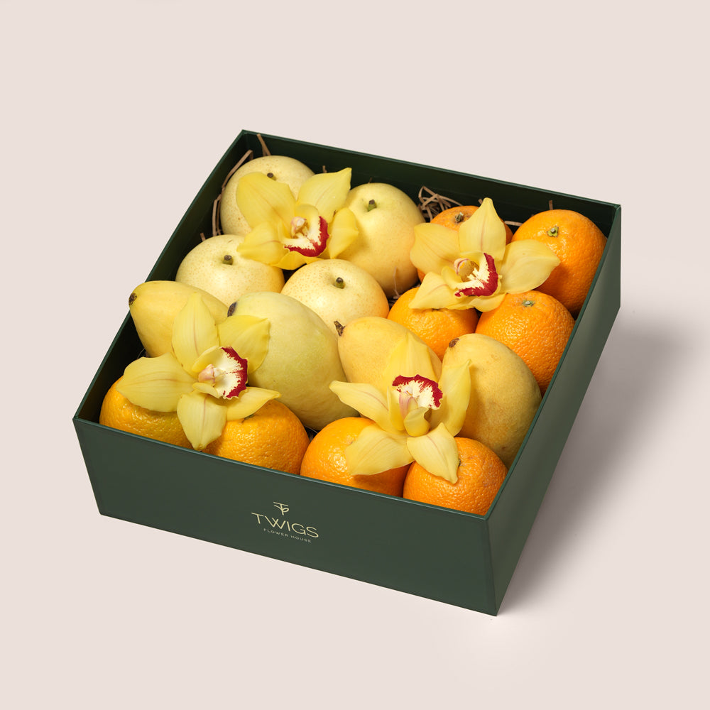 
TWIGS Citrus Box with fresh oranges, yellow mangoes, white pears and yellow cymbidium orchids in a dark green gift box, Dubai UAE