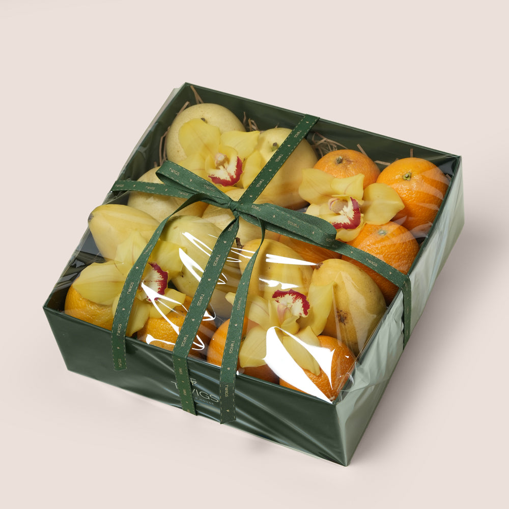 
TWIGS Citrus Box with fresh oranges, yellow mangoes, white pears and yellow cymbidium orchids in a dark green gift box, Dubai UAE