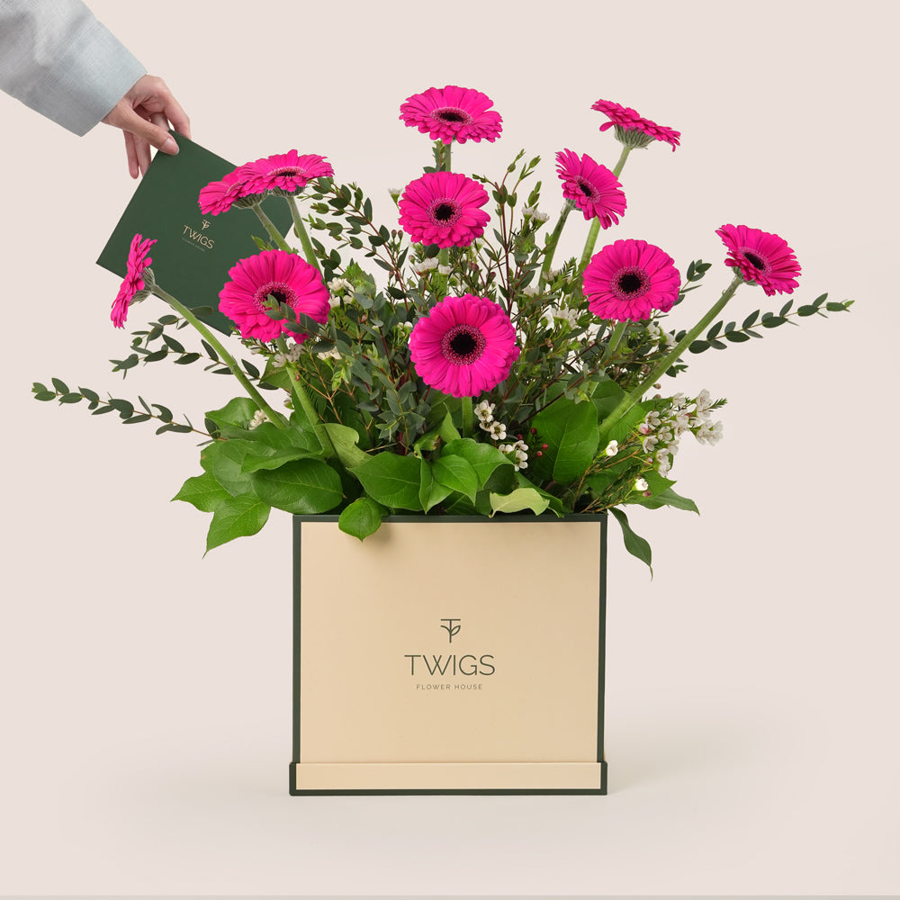 Fuchsia gerbera flower arrangement with fresh greenery in a TWIGS beige or green square box, available for same day flower delivery in Dubai when you buy flowers online.