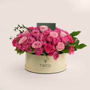 Grande round flower box with fuchsia cerise spray roses, fuchsia Ecuador garden roses, and light pink garden roses in TWIGS beige or green packaging, available for same day flower delivery in Dubai when you buy flowers online.