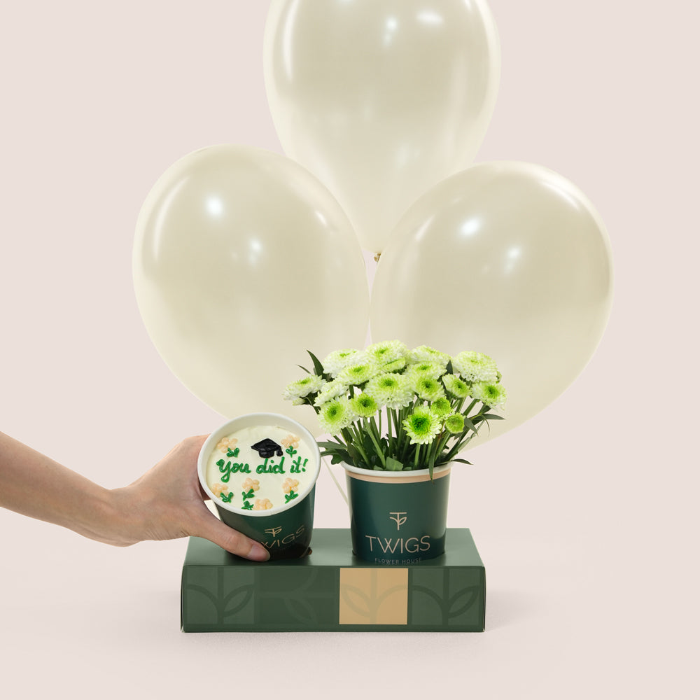 

Graduation combo with green flowers in TWIGS cup, chocolate cupcake with "You did it!" topper, and three white chrome balloons — TWIGS UAE