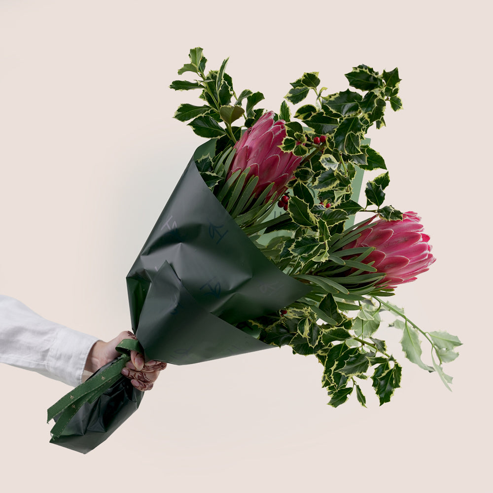 Bouquet of pink protea flowers and greenery held by a person against a beige background