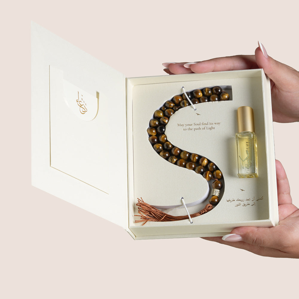 Tiger Eye misbaha beads shaped in an S beside Sakina perfume oil bottle in open cream gift box, TWIGS x Light of Sakina collaboration
