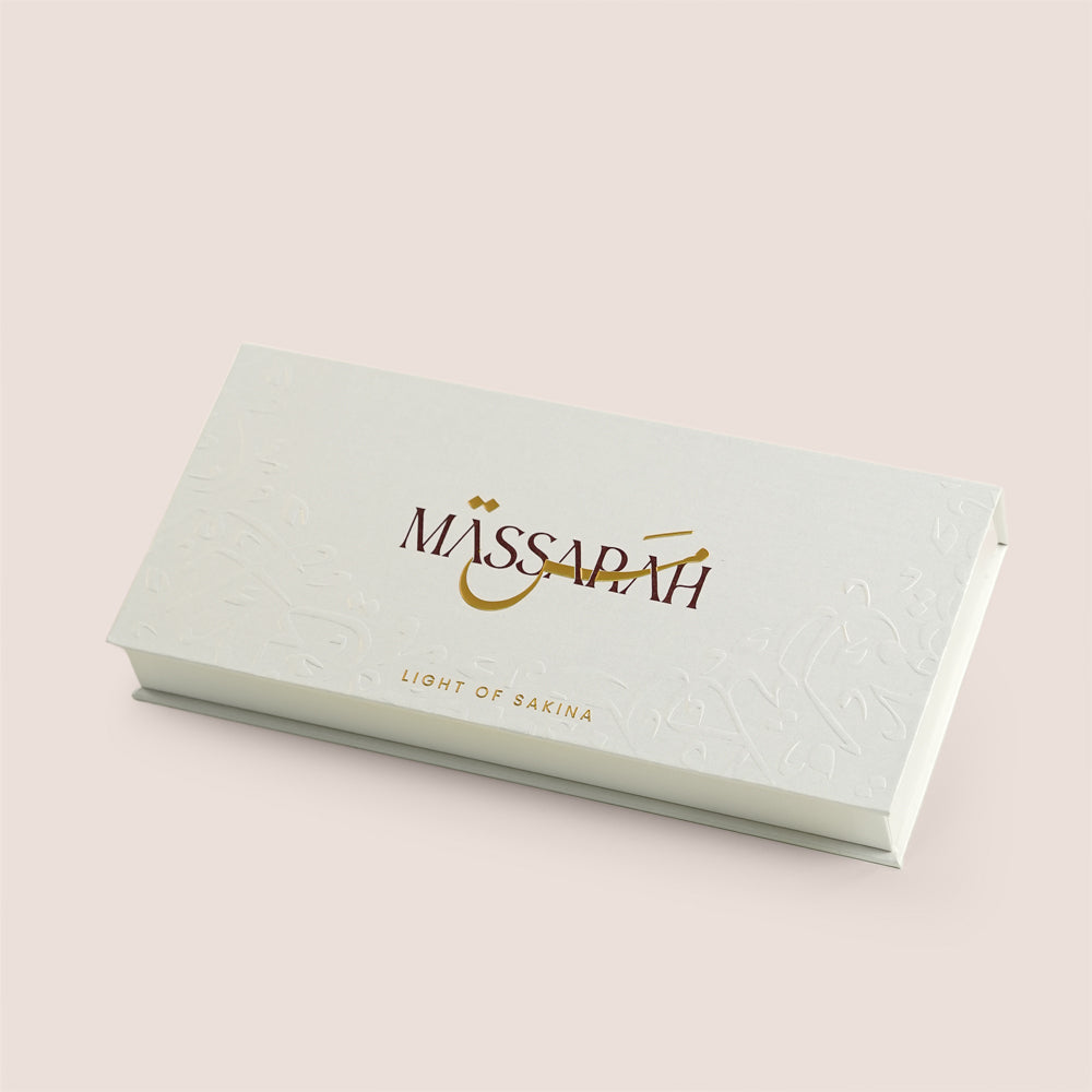 Five Massarah perfume oil bottles in an open beige box beside a gold scent guide card, TWIGS x Light of Sakina collaboration
