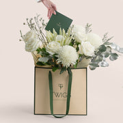 Floral arrangement in a Twigs Flower House bag with a hand holding a card on a light pink background