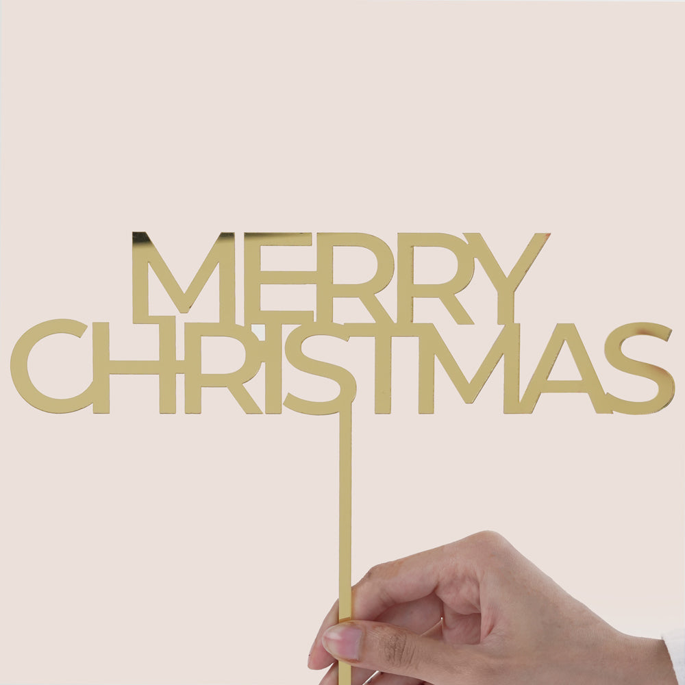 Hand holding a gold 'Merry Christmas' sign against a beige background