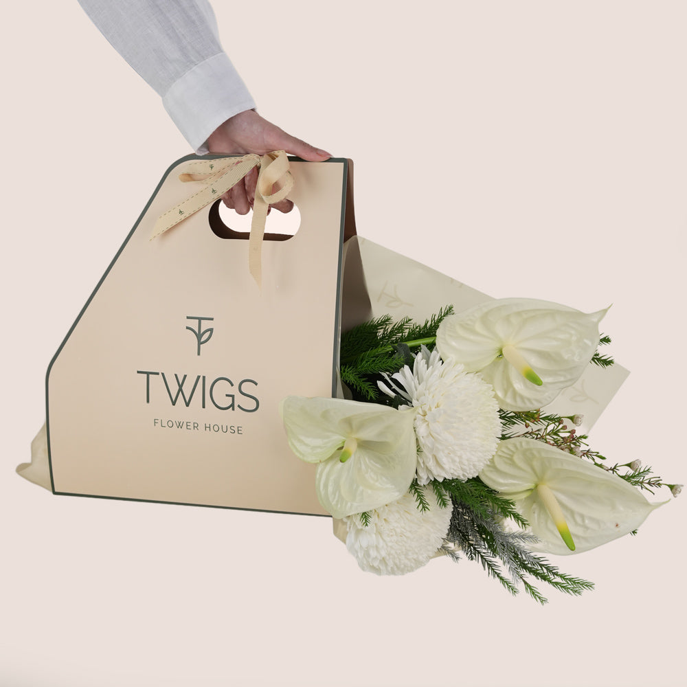bouquet of white flowers, including large white anthuriums and chrysanthemums, wrapped with greenery inside.