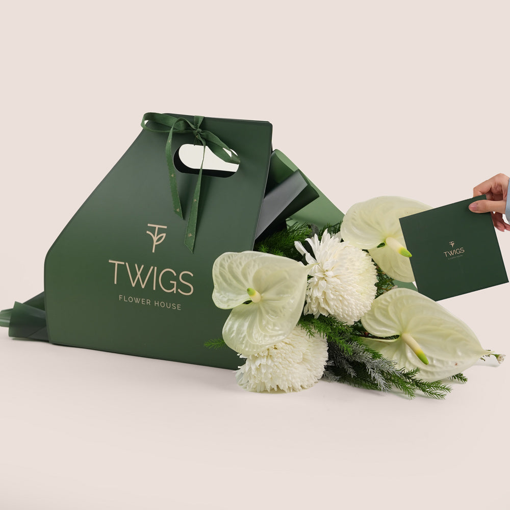 bouquet of white flowers, including large white anthuriums and chrysanthemums, wrapped with greenery inside.