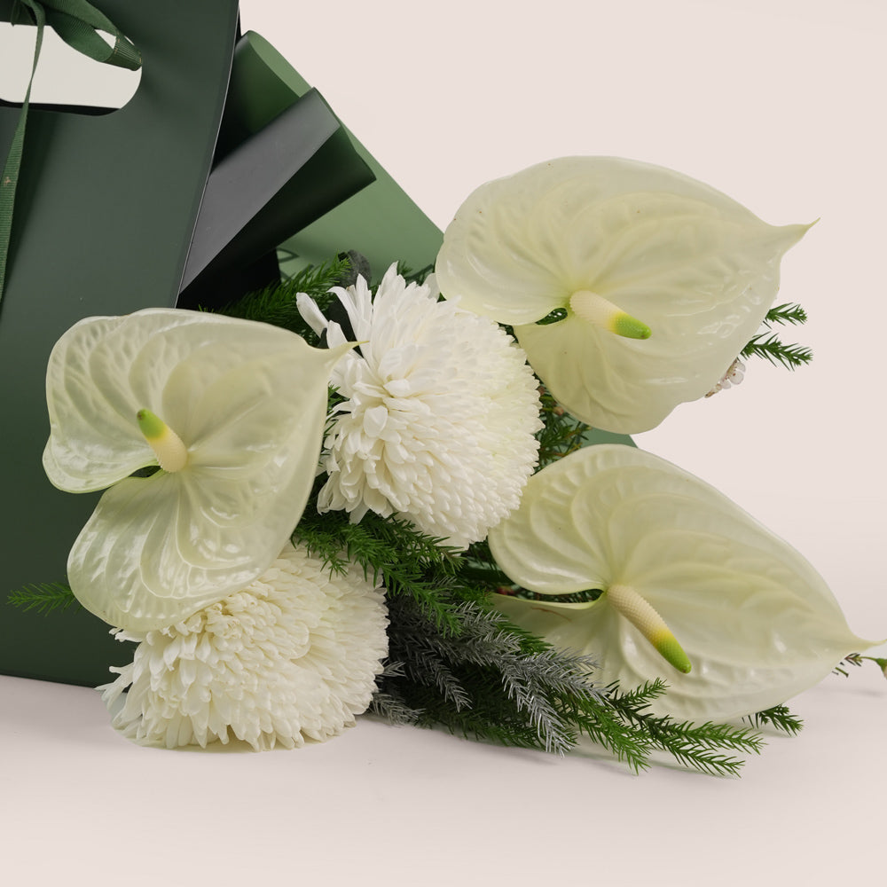 bouquet of white flowers, including large white anthuriums and chrysanthemums, wrapped with greenery inside.
