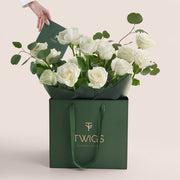 Green gift bag with white roses and TWIGS branding on a light beige background
