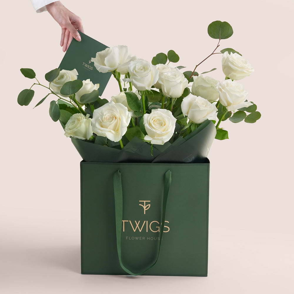 Green gift bag with white roses and TWIGS branding on a light beige background