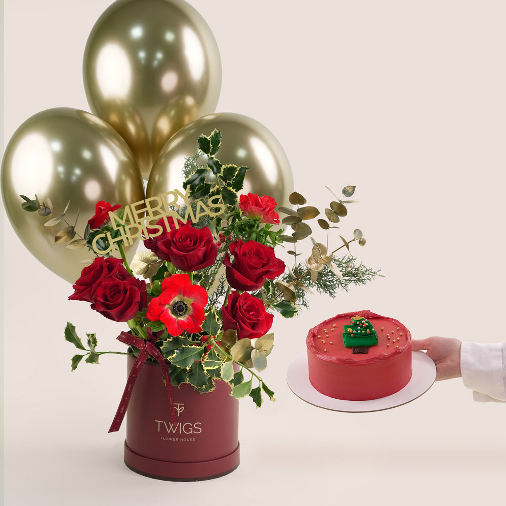 Christmas-themed arrangement with red roses, gold balloons, and a red cake on a white background.