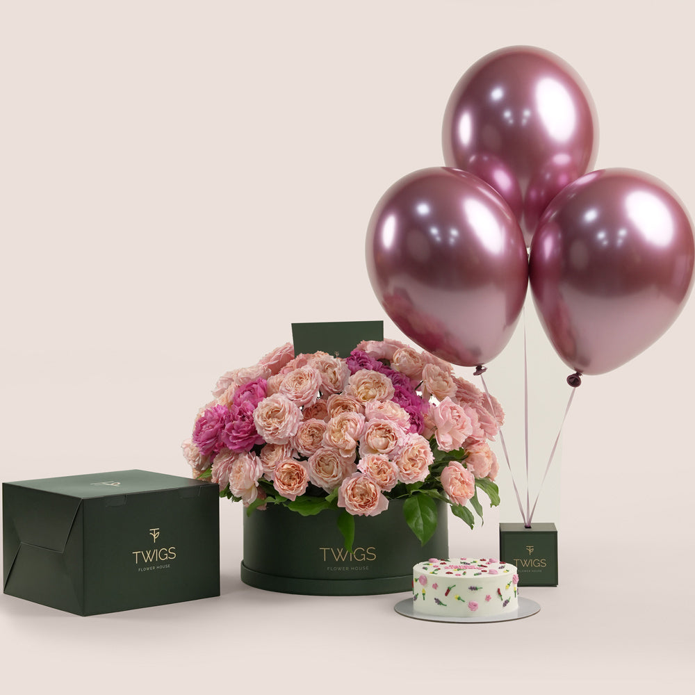 Grande round flower box with peach Juliet spray roses and cerise accents, paired with a 1kg birthday cake and three chrome dark pink balloons in TWIGS beige or green packaging, available for same day flower delivery in Dubai when you buy flowers online.