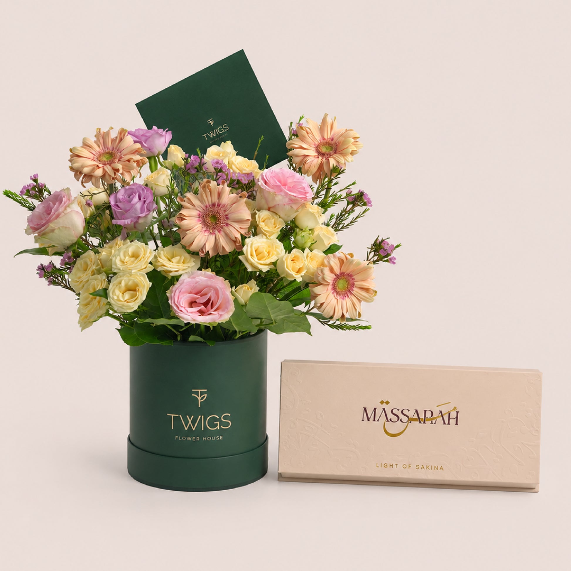 Peach gerberas, lisianthus and roses in a TWIGS round box beside a Massarah Her perfume oil set, TWIGS x Light of Sakina collaboration