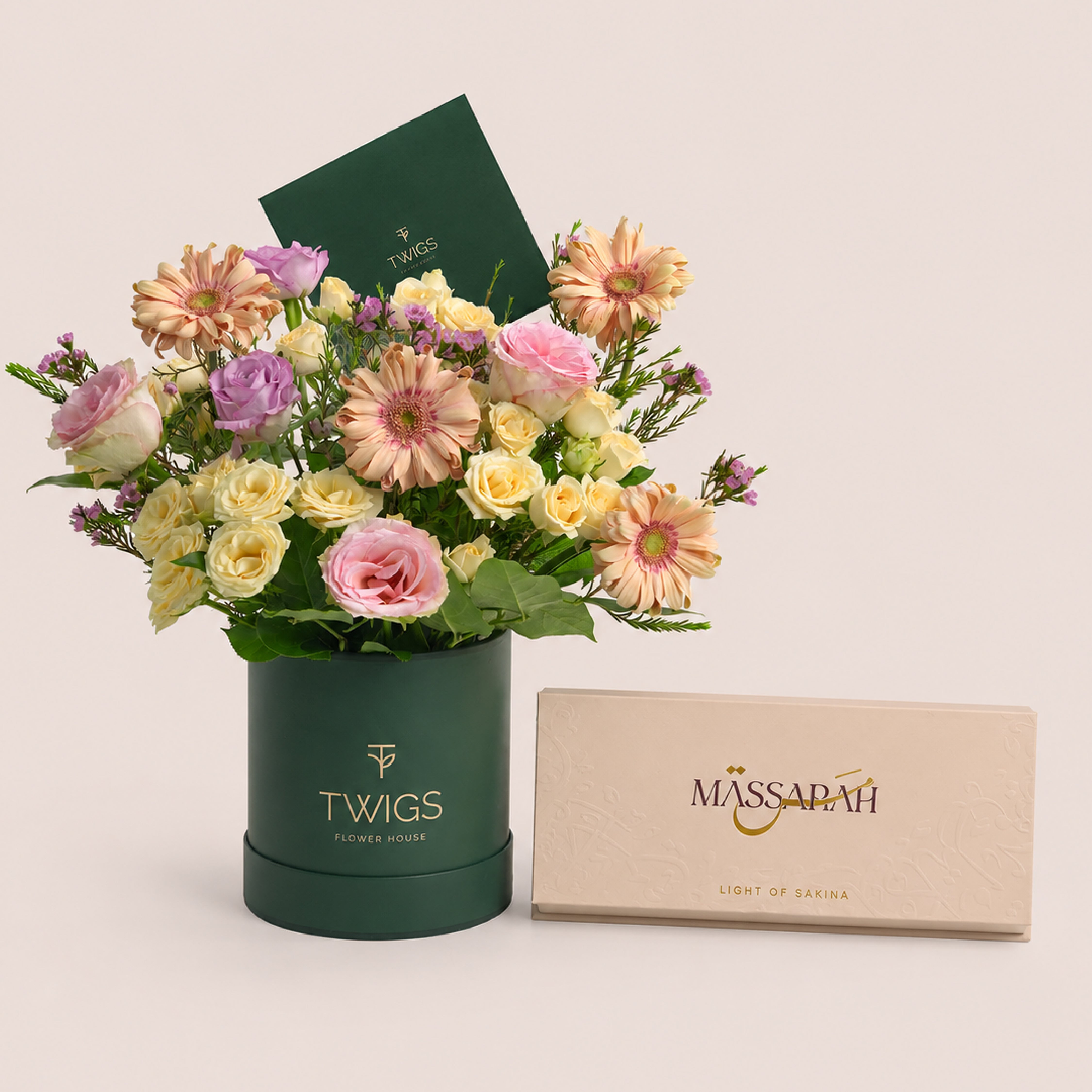 Peach gerberas, lisianthus and roses in a TWIGS round box beside a Massarah Her perfume oil set, TWIGS x Light of Sakina collaboration