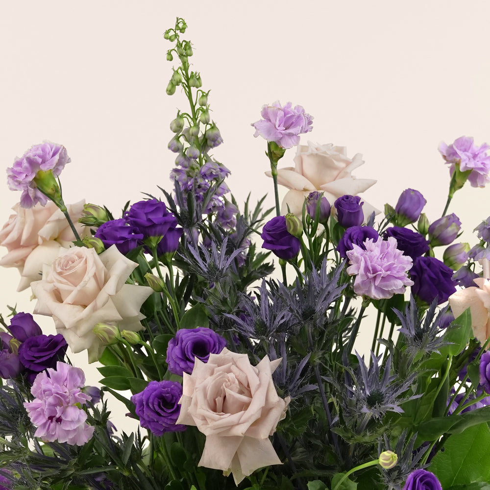 Grande round flower box with quicksand roses, purple lisianthus, carnations, delphiniums, and eryngium in TWIGS beige or green packaging, available for same day flower delivery in Dubai when you buy flowers online.