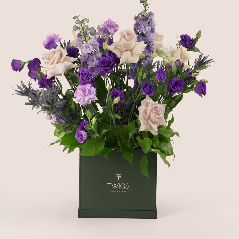 Square flower box with quicksand roses, purple lisianthus, light purple carnations, delphiniums, and eryngium in TWIGS beige or green packaging, available for same day flower delivery in Dubai when you buy flowers online.
