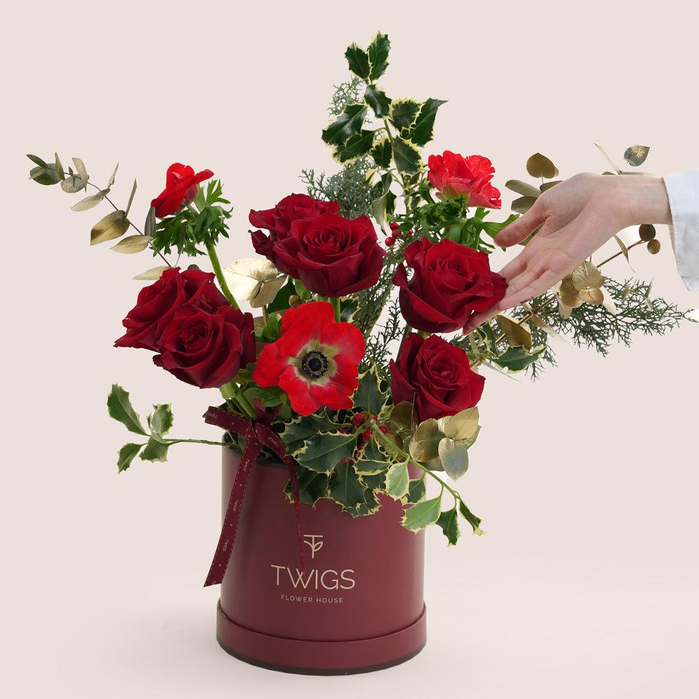 Bouquet of red roses and red anemone in a Twigs container on a beige background. Christmas_flowers_near_me_Dubai