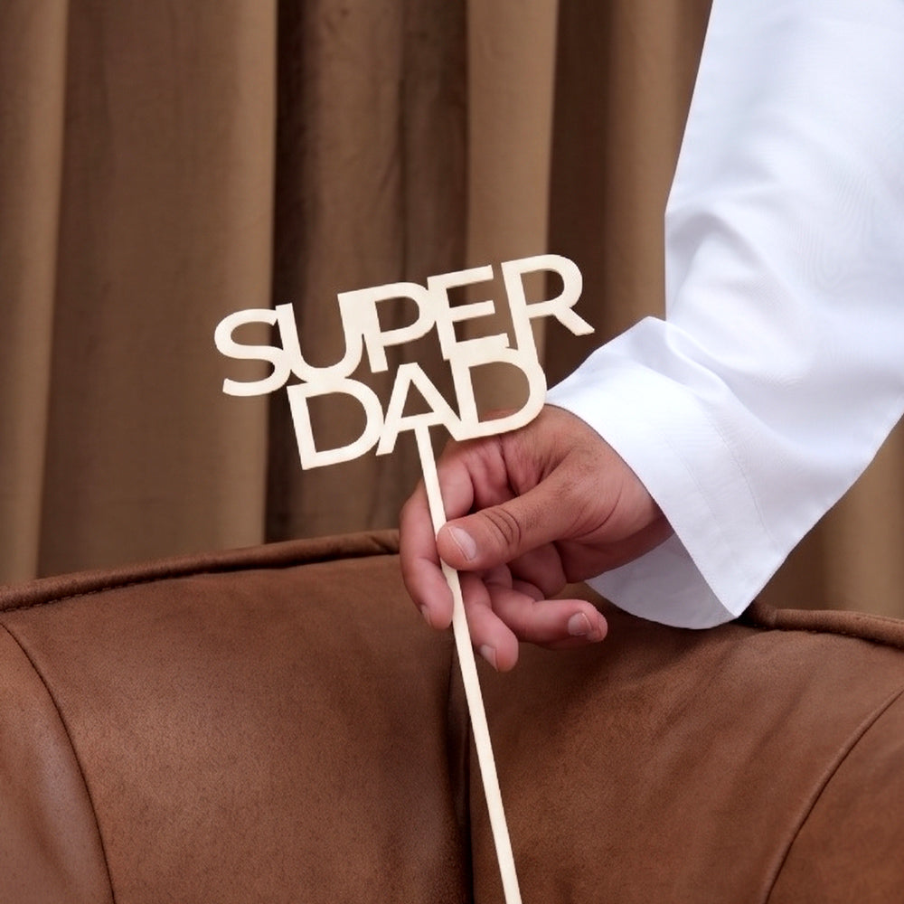Father's Day message topper reading Super Dad held against a brown curtain background, TWIGS flower arrangement add-on Dubai