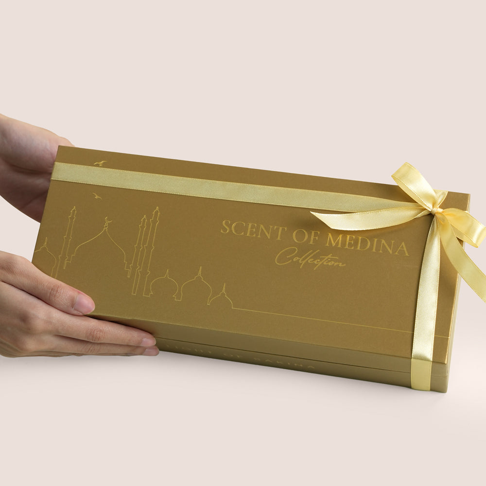 Three white Scent of Medina candles with gold Arabic calligraphy beside gold gift box, TWIGS x Light of Sakina collaboration