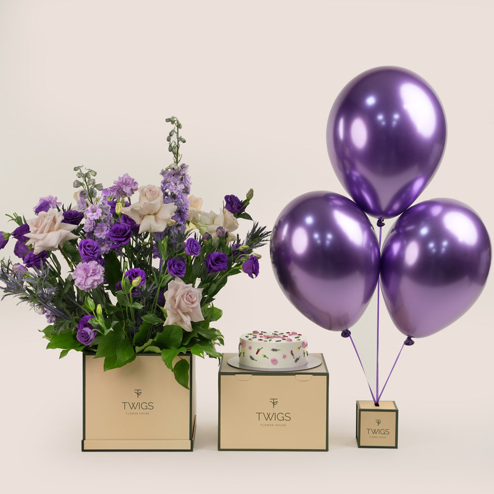 Subtle Bloom square flower box with quicksand roses and purple lisianthus, paired with a 1kg birthday cake and three purple chrome balloons in TWIGS beige or green packaging, available for same day flower delivery in Dubai when you buy flowers online.
