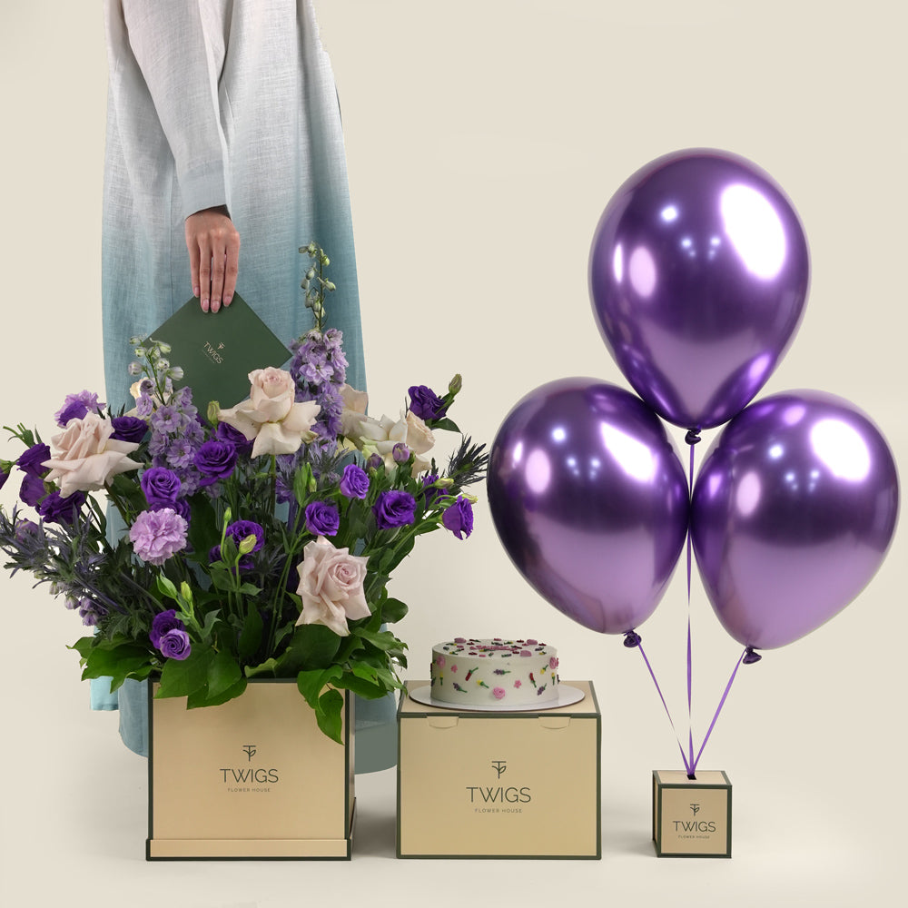 Subtle Bloom square flower box with quicksand roses and purple lisianthus, paired with a 1kg birthday cake and three purple chrome balloons in TWIGS beige or green packaging, available for same day flower delivery in Dubai when you buy flowers online.